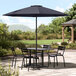A Lancaster Table & Seating indigo blue umbrella over a table and chairs on a patio.