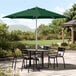 A table and chairs under a Lancaster Table & Seating green umbrella on a patio.