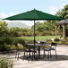 A Lancaster Table & Seating black table and chairs under a forest green umbrella on a patio.