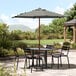 A Lancaster Table & Seating round black and white striped umbrella over a table and chairs on a patio.