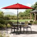 A black table and chairs under a red Lancaster Table & Seating umbrella on a stone patio.