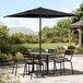 A Lancaster Table & Seating black umbrella over a table with chairs on a patio.