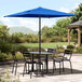 A black table and chairs under a blue Lancaster Table & Seating umbrella.