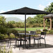 A table with black chairs under a black Lancaster Table & Seating umbrella on a stone patio.