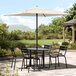 A black table and chairs under a Lancaster Table & Seating ivory umbrella on a stone patio.