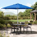 A table and chairs under a blue Lancaster Table & Seating umbrella on a stone patio.