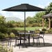 A Lancaster Table & Seating black umbrella over a table and chairs on a stone patio.