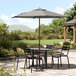 A Lancaster Table and Chairs under a Lancaster Table & Seating Graphite Woodgrain Aluminum Umbrella on a stone patio.