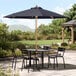 A Lancaster Table & Seating indigo blue umbrella over a table and chairs on a stone patio.