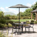 A table with four black chairs and a Lancaster Table & Seating black umbrella on a patio.