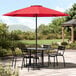 A black table with black chairs and a red Lancaster Table & Seating umbrella.