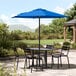 A black table and chairs on a patio with a blue Lancaster Table & Seating umbrella.