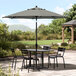 A table and chairs under a black and white striped Lancaster Table & Seating umbrella on a patio.