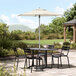 A Lancaster Table & Seating ivory umbrella over a table with chairs on a stone patio.