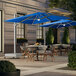 A Lancaster Table & Seating blue square cantilever umbrella with lights over a table and chairs on an outdoor patio.