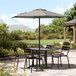 A Lancaster Table and Chairs under a black umbrella on a patio.