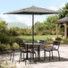 A Lancaster Table and Seating black square umbrella over a table with chairs on a stone patio.