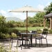 A Lancaster Table & Seating ivory umbrella on a table with chairs on an outdoor patio.