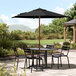 A black Lancaster Table & Seating umbrella on a patio table with chairs.