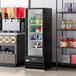 A black glass door merchandiser refrigerator with LED lighting, featuring a left-hinged swing door and stocked with beverages.