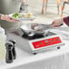 A woman cooking meat on an Avantco countertop induction range.