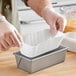 A gloved hand using a White Dry-Waxed Fluted Oblong Loaf Liner to bake a cake.