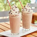 Two glasses of Dr. Smoothie Cafe Essentials Neutral Base milkshakes with whipped cream and straws on a table.