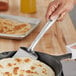 A person using a Choice stainless steel palta turner to cut a flatbread.