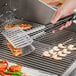 A person using Backyard Pro stainless steel fish tongs to cook food on a grill.