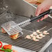 A person using Backyard Pro stainless steel fish tongs to cook shrimp on a grill.