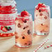 A glass of Dr. Smoothie Strawberry Acai Refresher with a straw and berries next to a jar of the juice.