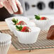 A gloved hand putting a strawberry in a white fluted baking cup.