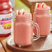 A glass jar of Dr. Smoothie Strawberry Banana fruit smoothie mix with a pink drink next to it.