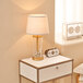 A Globe Fillable Ribbed Glass Table Lamp on a white nightstand next to a clock.