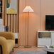 A Globe wood-toned floor lamp in a living room with a couch and a magazine.