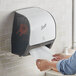 A person using a Scott white and black wall mount automatic paper towel dispenser.
