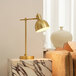 A Globe Vintage Matte Brass desk lamp with a gold base on a marble table next to a couch.