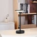 A black Globe Novogratz battery-powered LED table lamp with a frosted diffuser on a white table.