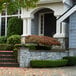 A matte black outdoor post mount light with clear glass panels on a rectangular frame next to a stone driveway.