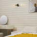 A white bedroom with a wood wall and a Globe Matte Black and Brass Vanity Light above a mirror.