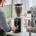 A man using a Mahlkonig white espresso grinder to grind coffee beans.