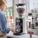 A woman using a Mahlkonig white espresso grinder to grind coffee beans.