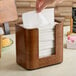 A person using a Tork walnut wood tabletop napkin dispenser to get a napkin.