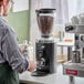 A man using a Mahlkonig black espresso grinder on a counter in a coffee shop.