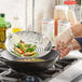 A person using a Town stainless steel mandarin skimmer to cook food in a wok on a stove.