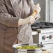 A person using a Choice chrome-plated round-faced potato masher with a wood handle to mash potatoes in a kitchen.