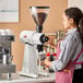 A woman using a Mahlkonig white coffee grinder in a professional kitchen.