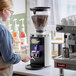 A woman using a Mahlkonig white espresso grinder on a counter.