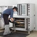 A man in a professional kitchen putting cookies in a Cooking Performance Group double deck convection oven.