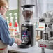 A woman using a Mahlkonig espresso grinder on a counter.